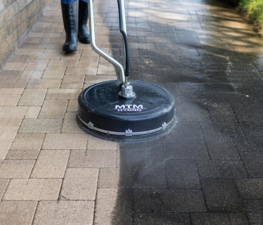 Pressure washer cutting a clean stripe through a concrete driveway